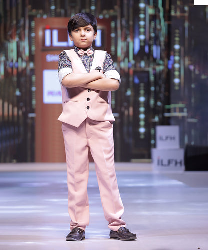 This boys party clothes set consists of a light pink Coloured waistcoat, matching pants and a self-printed shirt. It features a matching bow, a cute broach and a printed pocket square that uplifts the entire look.