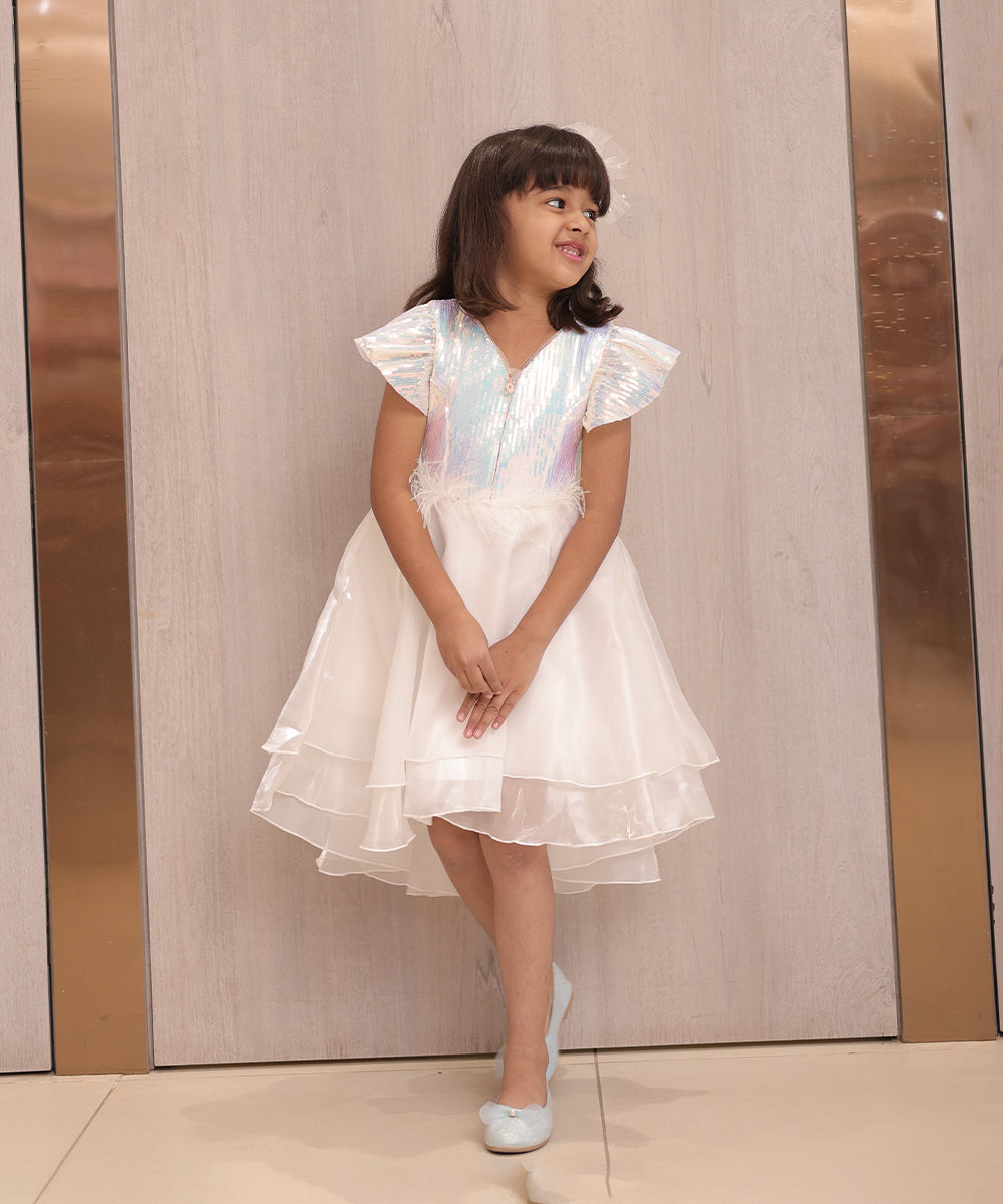 It's a cute white coloured up-and-down birthday frock with a back zip closure. A perfect marriage wears for girls. It features a bow on the back and beautiful feather detailing on the waist that uplifts the entire look.