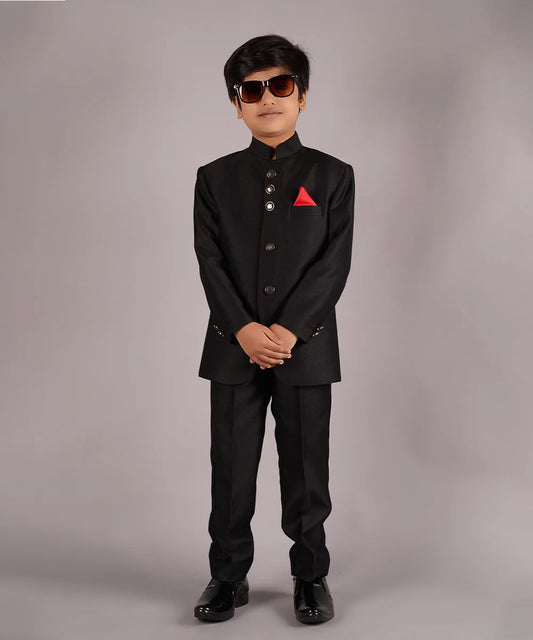 This classic black coloured Jodhpuri suit set is curated from high-quality self-textured fabric. This set has a coat that comes along with matching pants and a red Colored pocket square for boys.