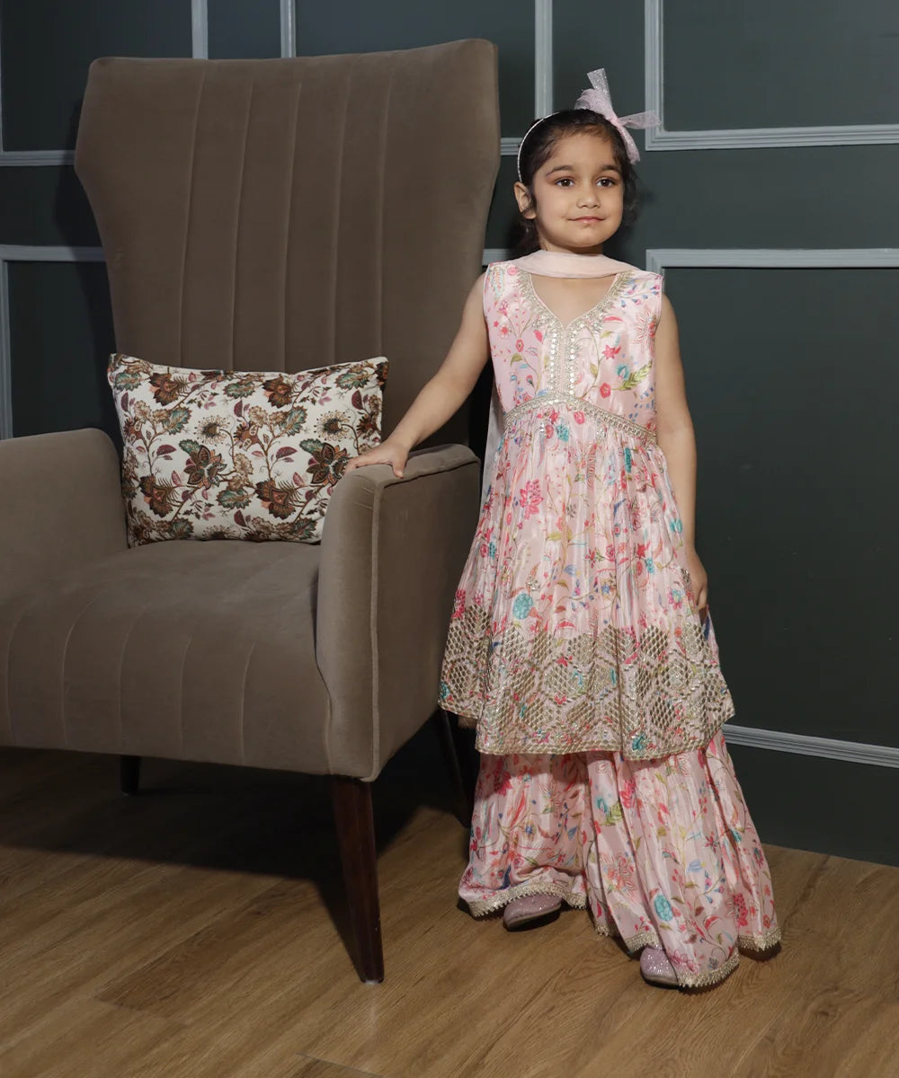 This baby girl pink colored sharara suit consists of a kurta with a back zip closure, a matching sharara and a dupatta.