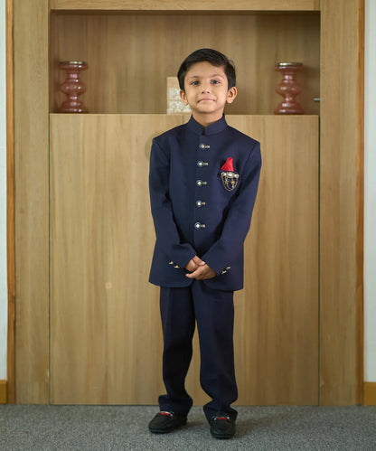 It is a beautiful navy blue coloured Jodhpuri suit for boys. It consists of a Jodhpuri Coat along with matching pants. It features a red coloured pocket square and a nice broach.