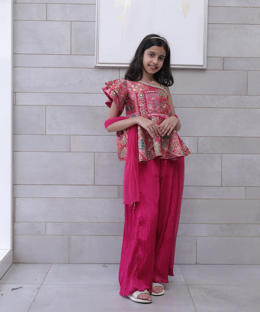 This rani pink coloured baby girl sharara suit consists of a peplum top with a back zip closure, a matching sharara and a dupatta. It features an embellished neck and tassels on the dupatta.